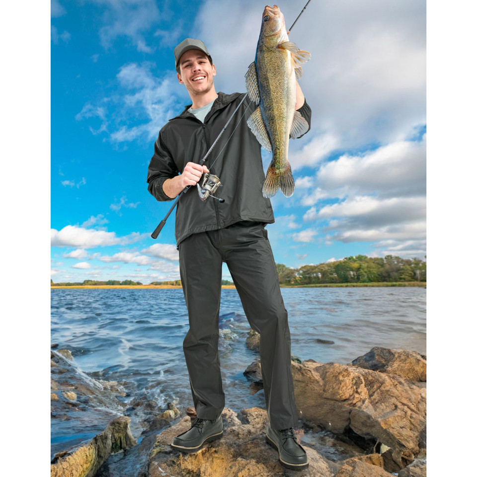 Charcoal grey waterproof rain pants with elasticated waist worn outdoors by angler holding fishing rod and catch