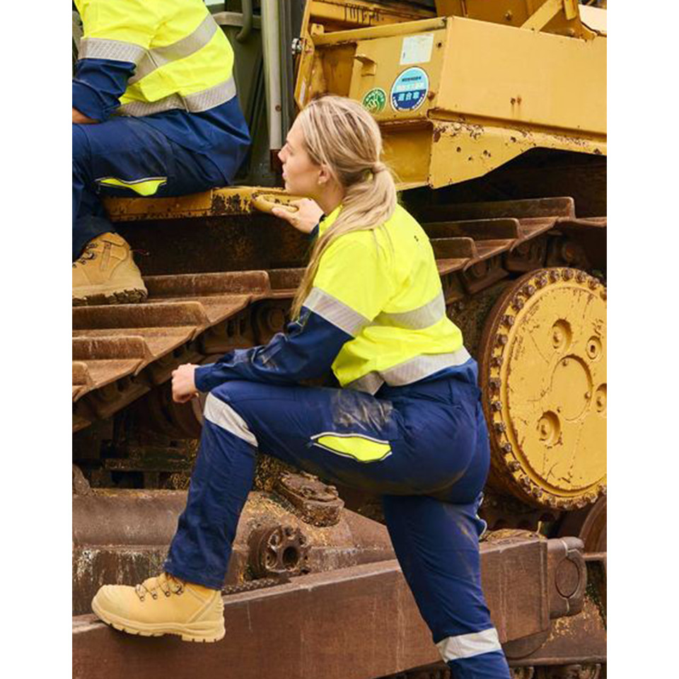 Woman in hi vis yellow and navy taped stretch ripstop shirt climbing heavy machinery on worksite