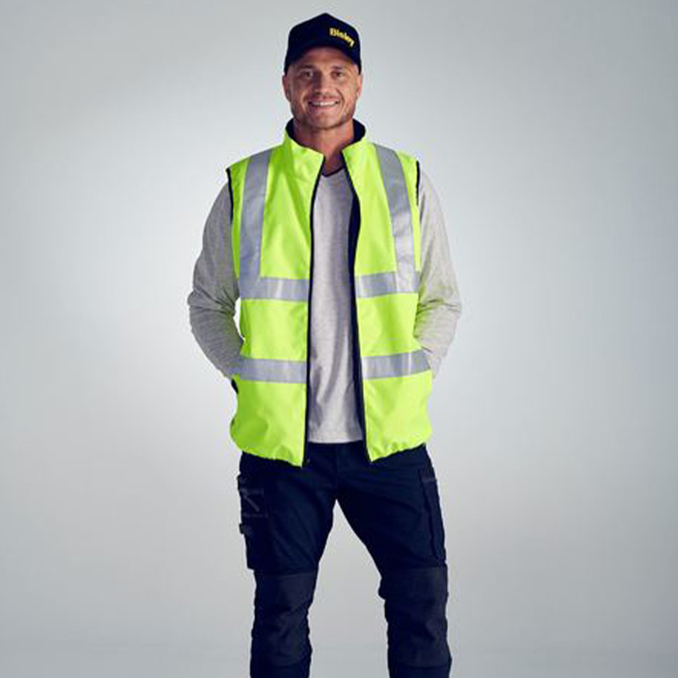 Man wearing fluoro yellow hi vis reversible puffer vest with reflective tape, styled over grey long sleeve and dark cargo pants