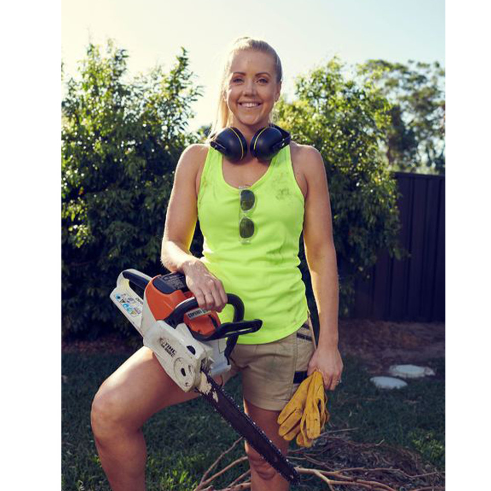 Woman in fluoro yellow racer back singlet with dark side panels, holding chainsaw outdoors