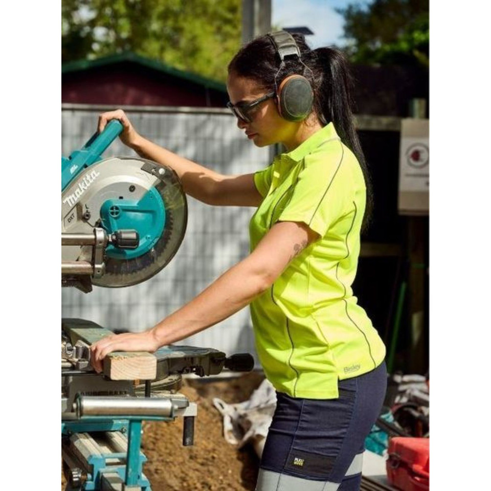 Woman operating a drop saw on a worksite wearing a hi-vis yellow polo with reflective piping and short sleeves