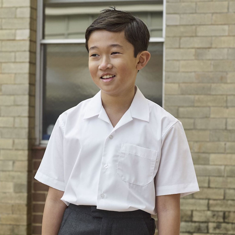 Boy wearing white short sleeve school shirt with open neck collar and chest pocket, school courtyard setting
