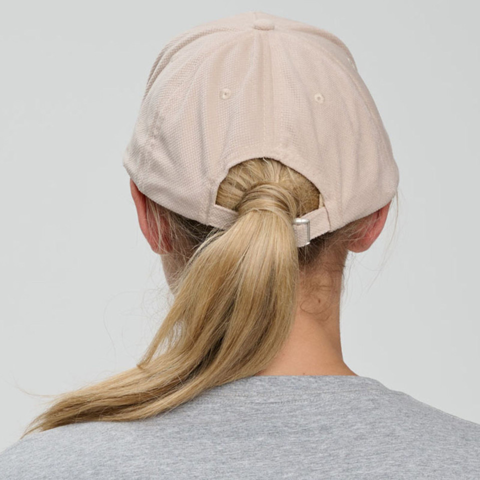 Soft pink five panel cap with adjustable back strap shown from rear on blonde model