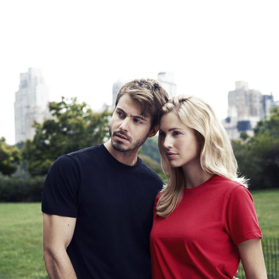 Man in black crew neck tee and woman in red crew neck tee with short sleeves on grass with city skyline background