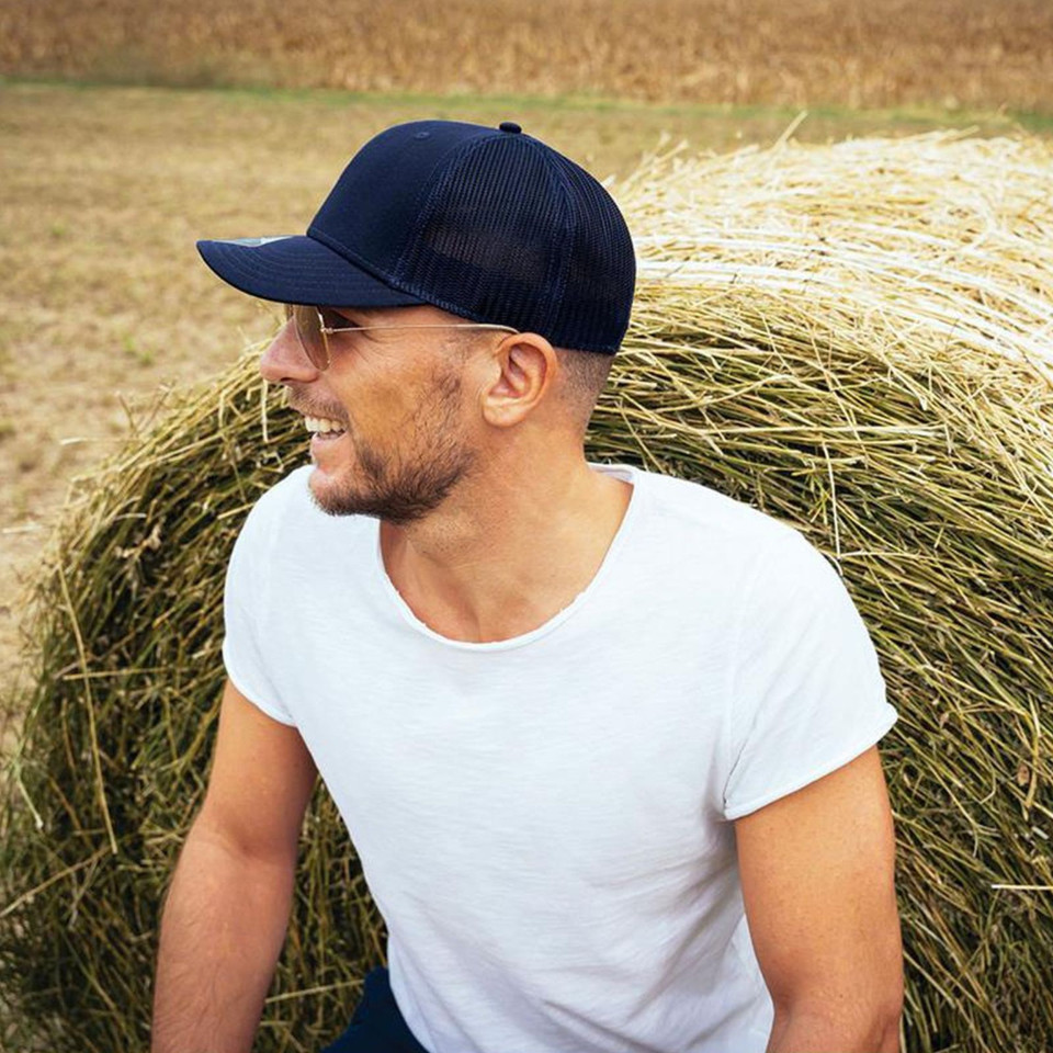 Man wearing navy blue trucker cap with mesh back panels, seated against hay bale outdoors