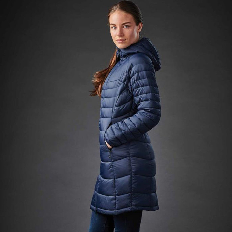 Woman wearing a navy blue quilted ¾ length parka with attached hood and side hand pockets