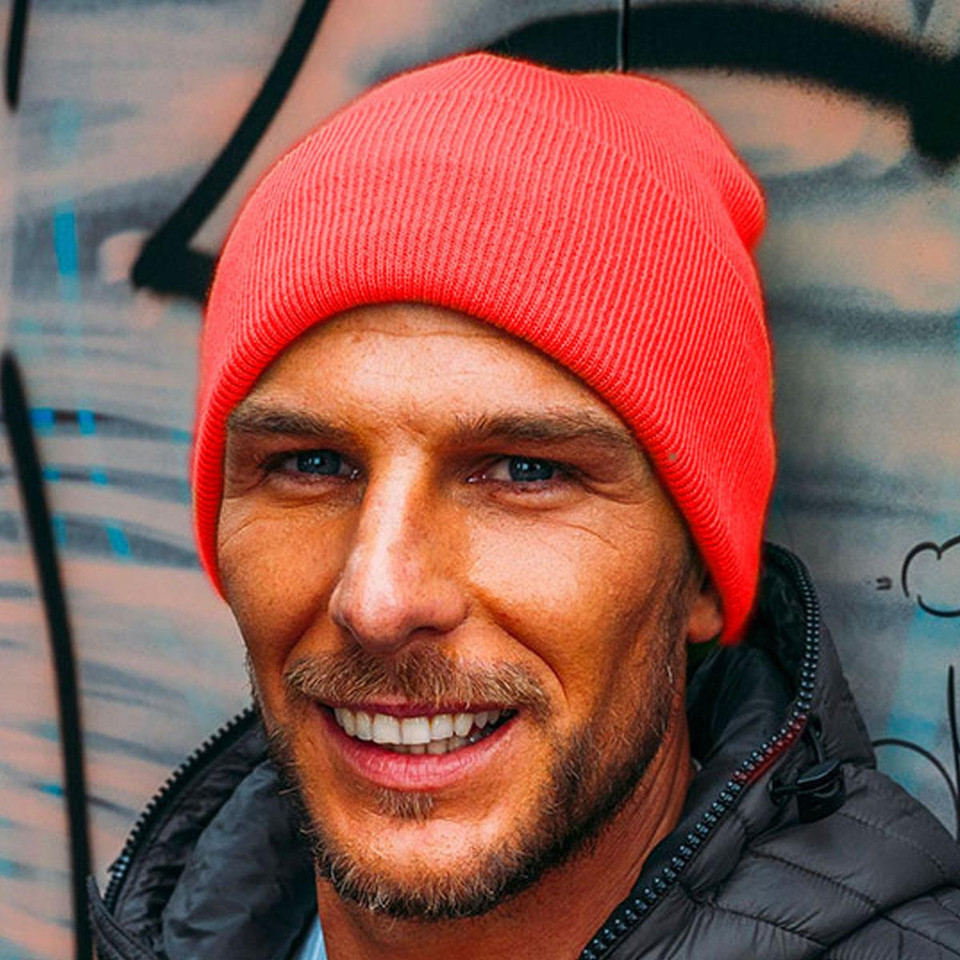 Man wearing a coral red fine-knit acrylic cuffed beanie against a graffiti wall