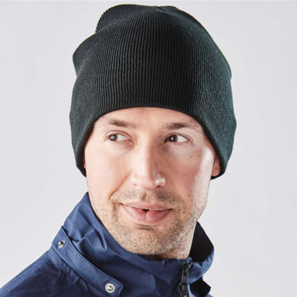 Man wearing a dark charcoal fine-knit stretch beanie with a navy zip-up jacket, outdoor setting