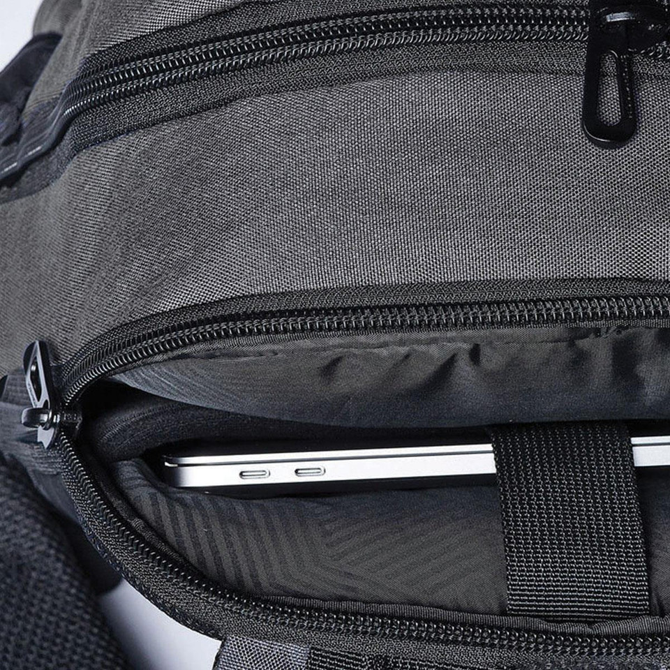 Close-up of charcoal grey backpack showing open laptop compartment with slim silver laptop and black zip detailing