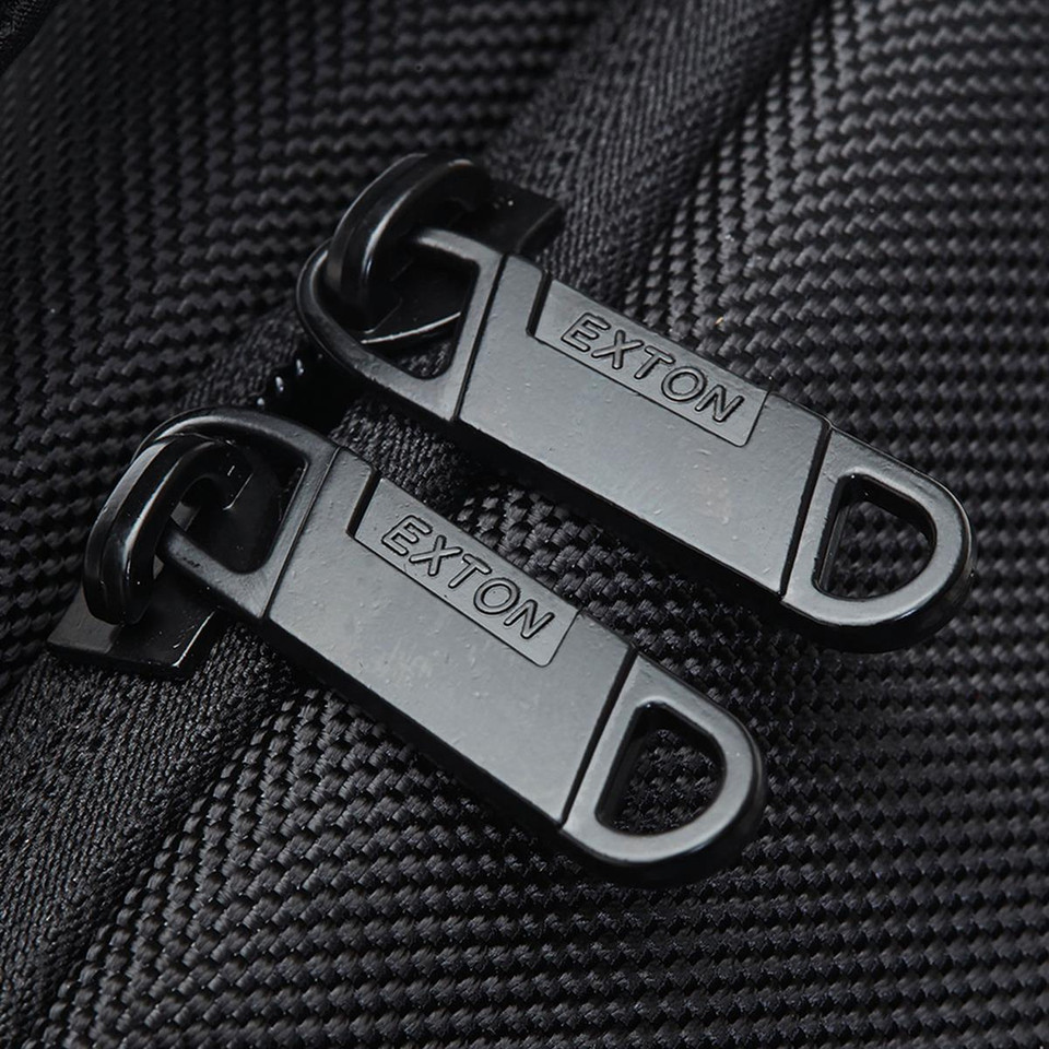 Close-up of two matte black branded zip pullers on black textured ripstop fabric panel