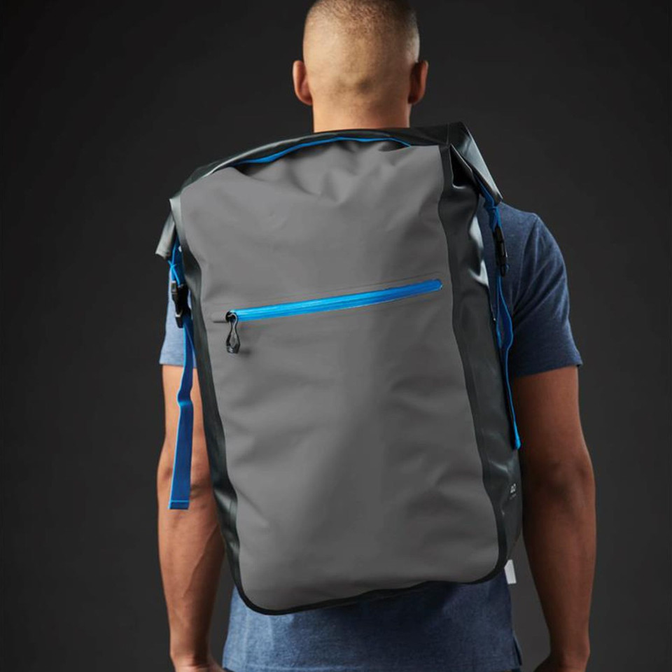 Man wearing charcoal roll-top waterproof backpack with cobalt blue zip pocket and shoulder straps
