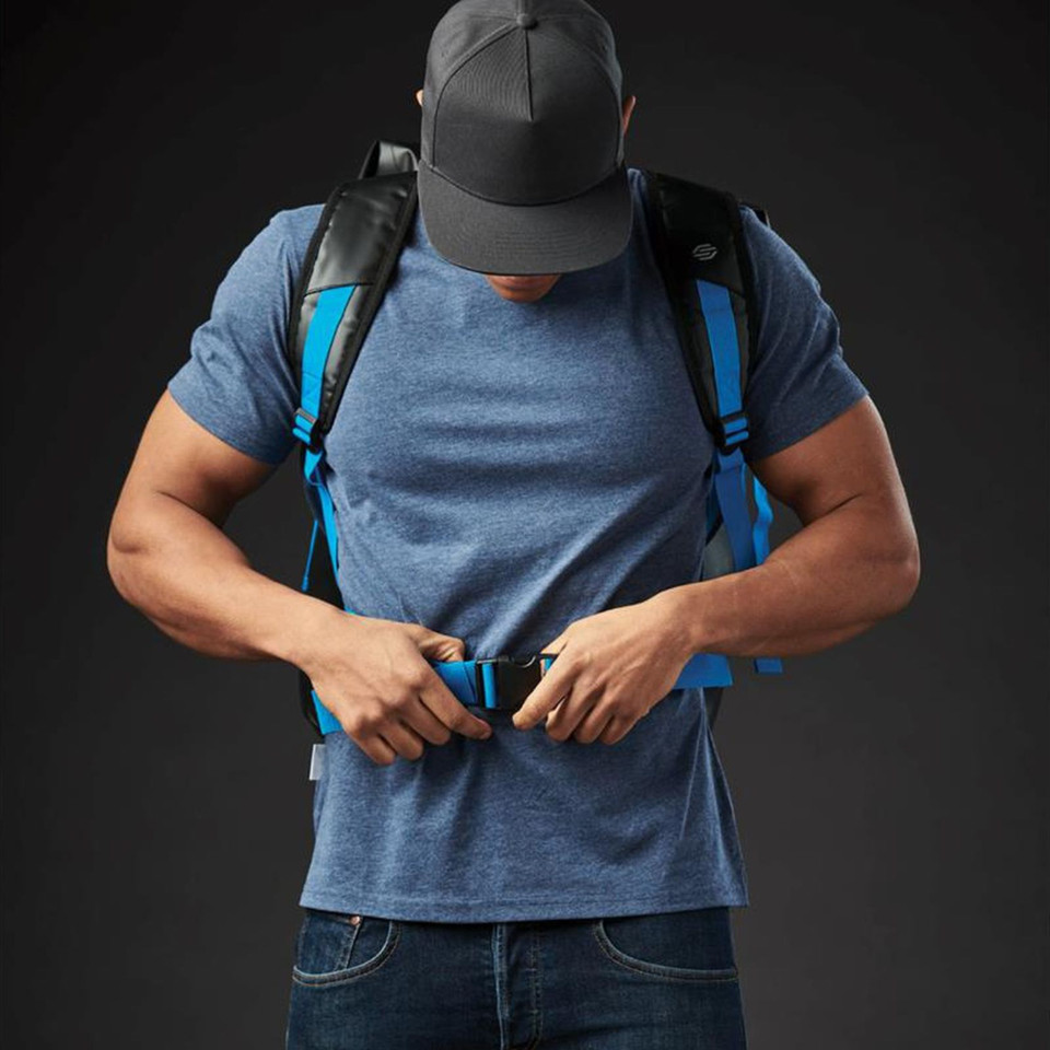 Model wearing Stormtech 40L waterproof roll-top backpack in cyan and black with chest strap fastened