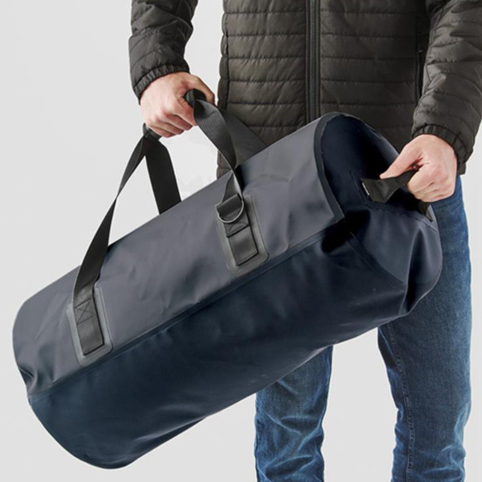 Model holding large navy blue waterproof duffel bag with welded seams and black carry handles