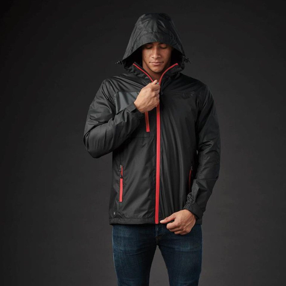 Man wearing graphite waterproof shell jacket with red zip contrast, adjustable hood, and side zip pockets