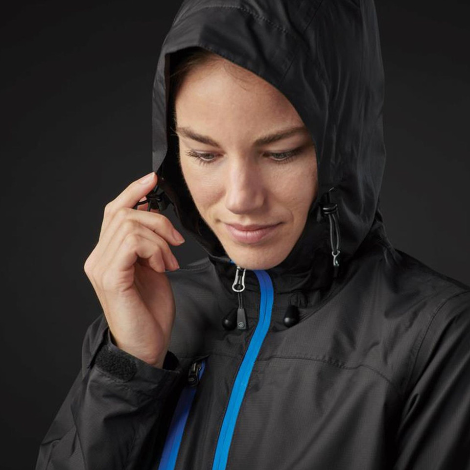 Woman wearing black waterproof shell jacket with royal blue contrast zip and structured hood with drawcord adjusters