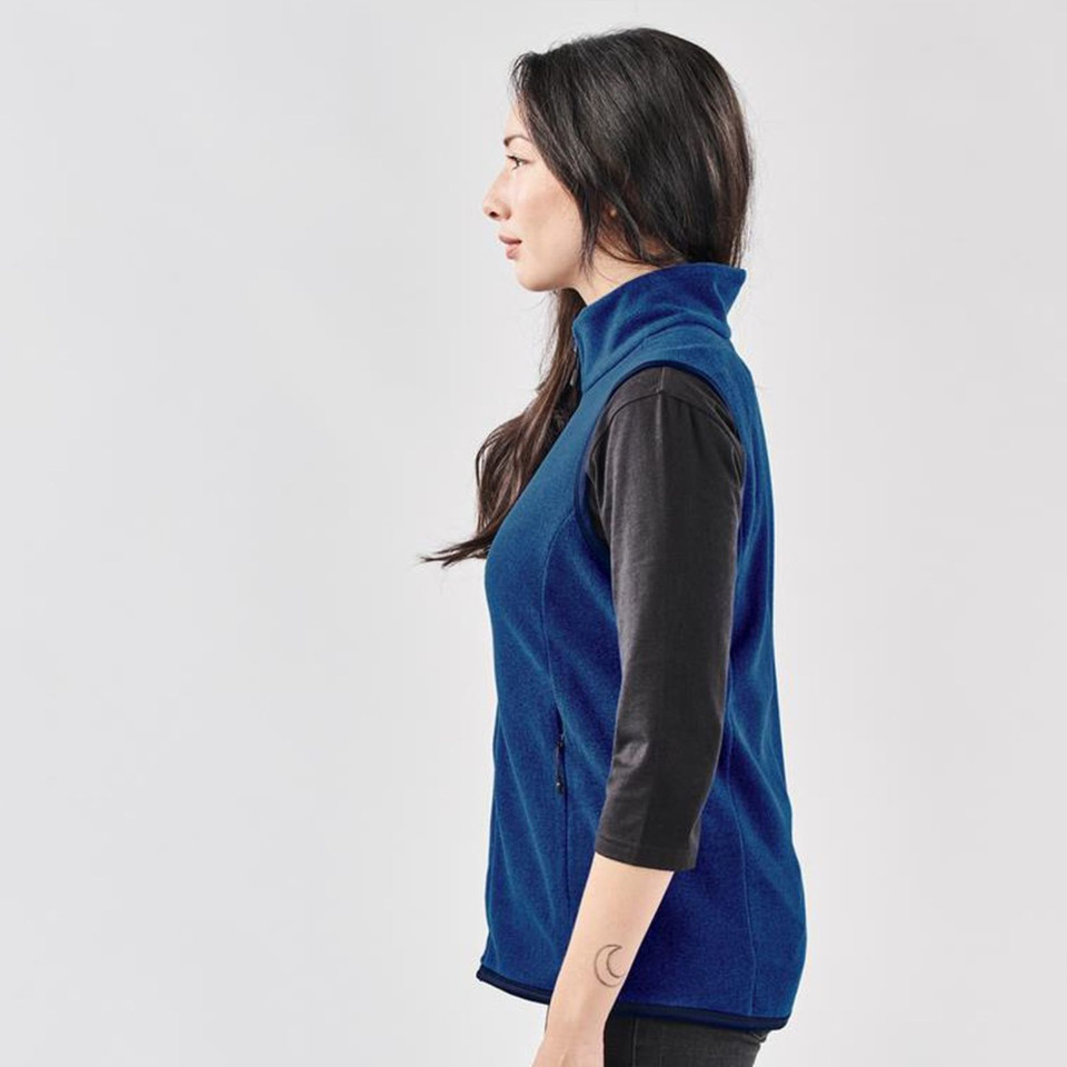 Woman wearing navy blue fleece vest with stand collar and side zip pockets over black long-sleeve top, side profile view