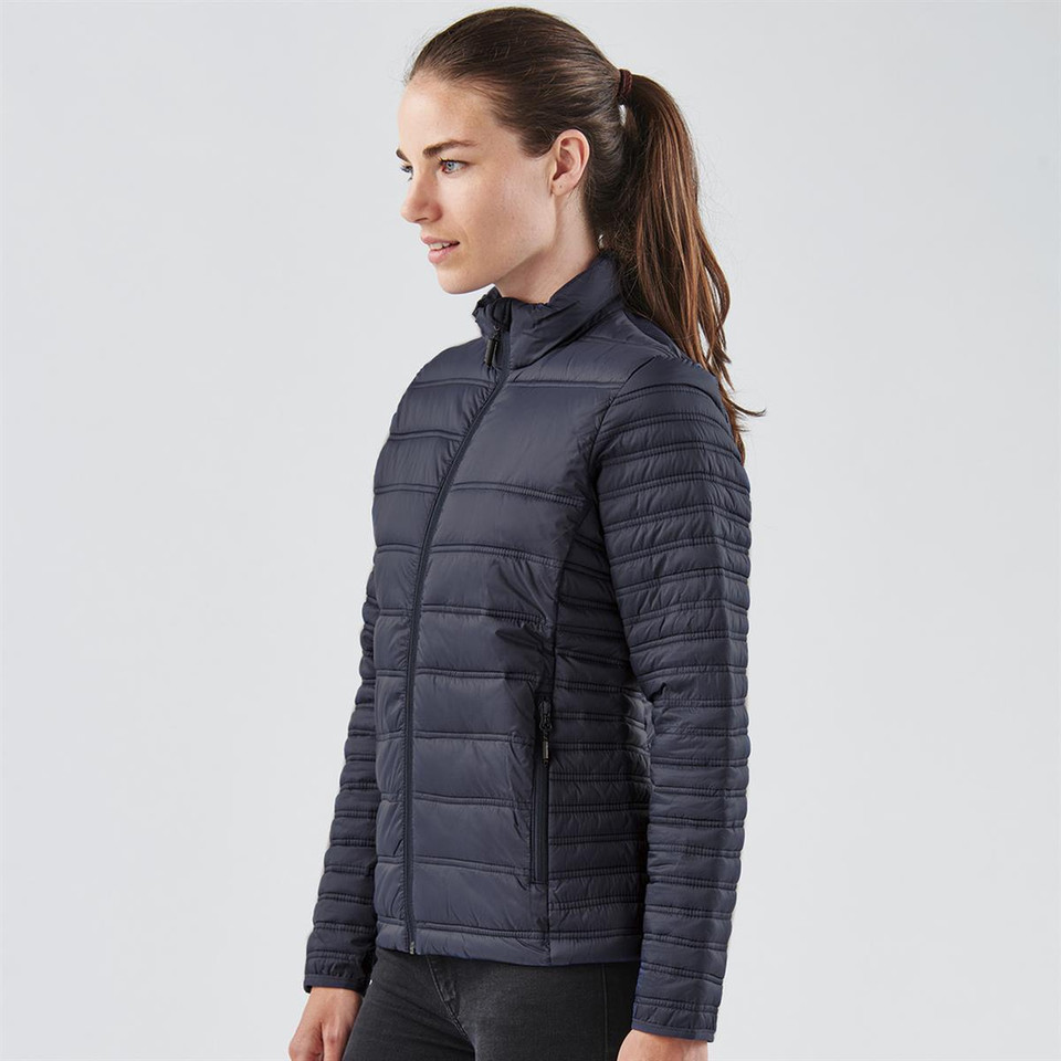 Woman wearing navy quilted puffer jacket with stand collar, zip front, and horizontal baffle stitching