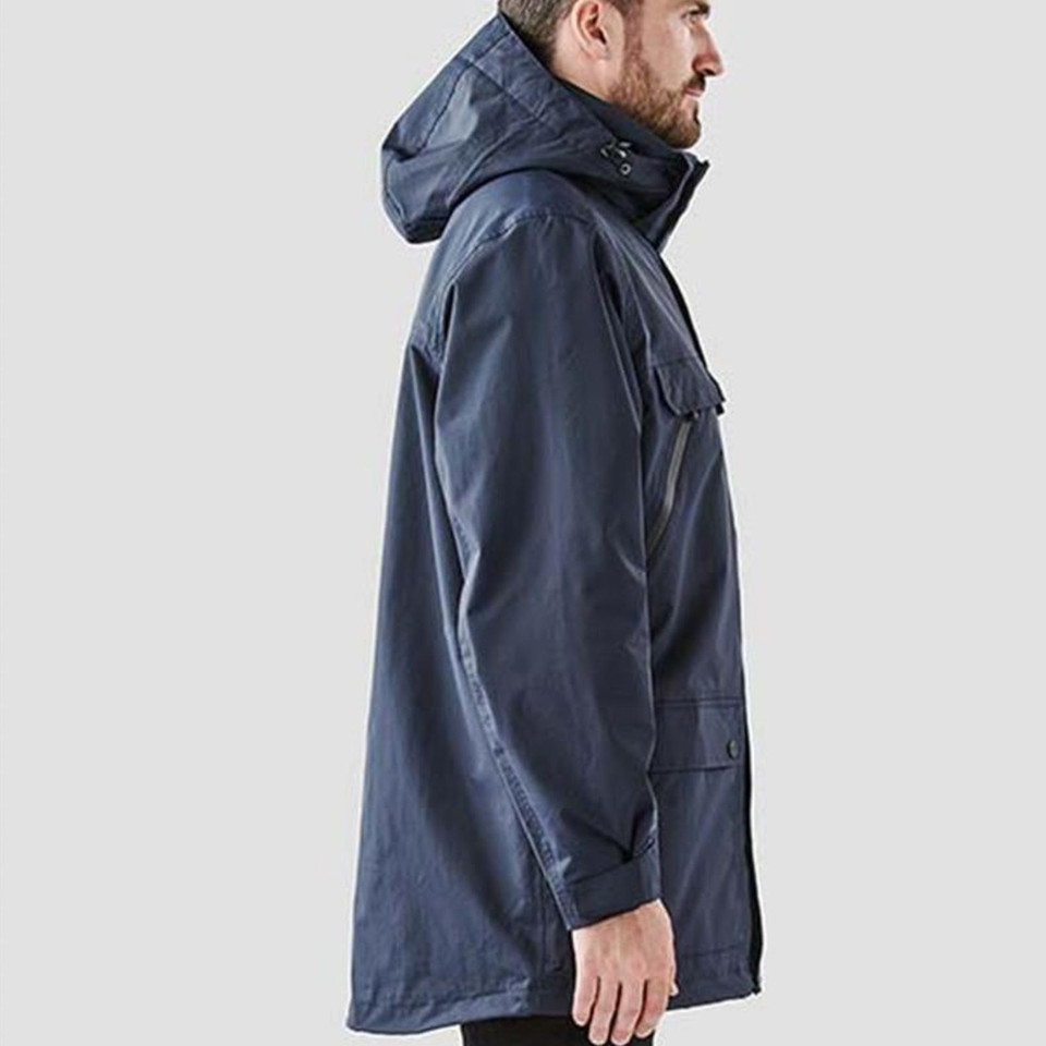 Man wearing navy long-line hooded waterproof jacket, side view showing zip chest pocket and lower flap pocket