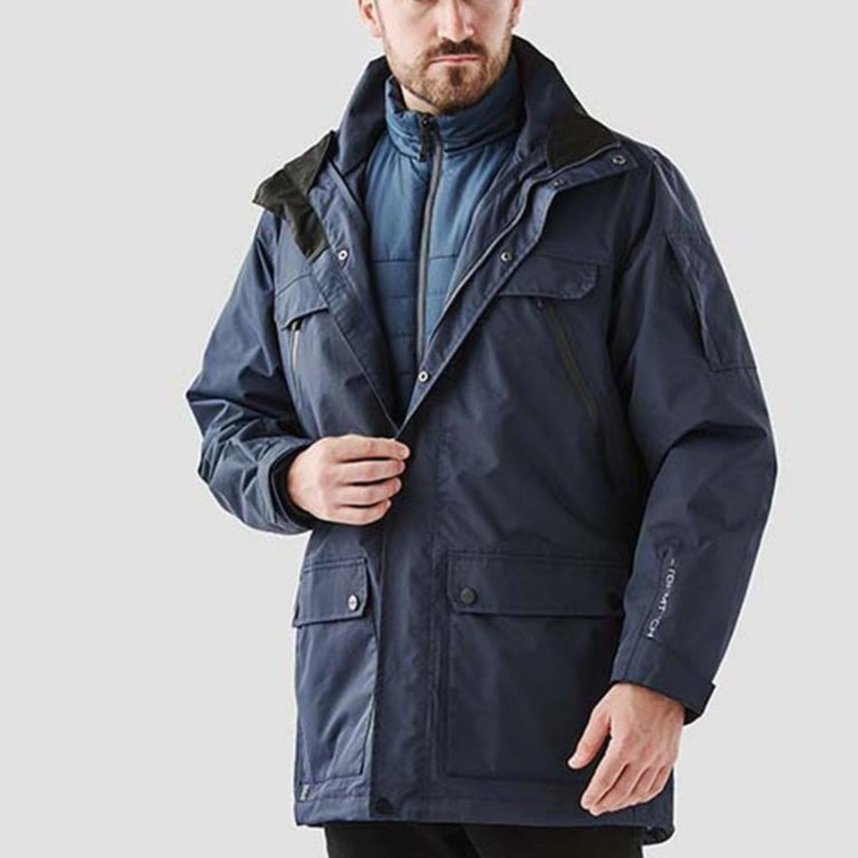 Man wearing navy 3-in-1 system jacket with black contrast hood, chest pockets, and quilted inner layer visible