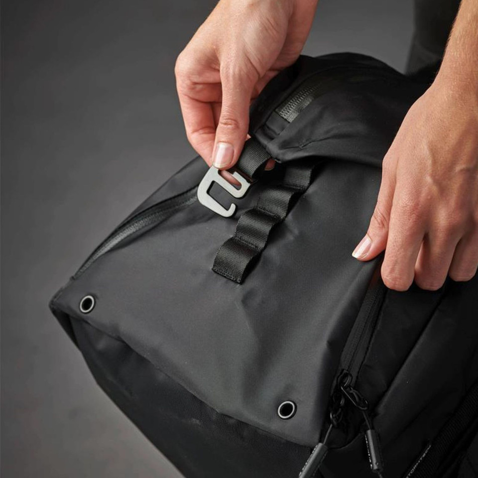 Close-up of hands fastening silver clip buckle on black nylon duffle bag with webbing strap and metal eyelet detail
