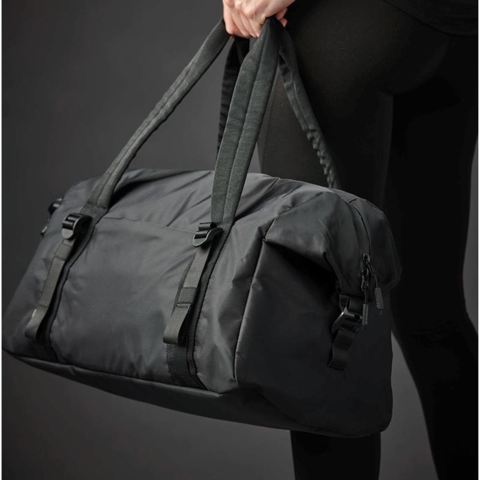 Charcoal grey 32L nylon duffle bag with buckle straps and zip pocket held by model in black
