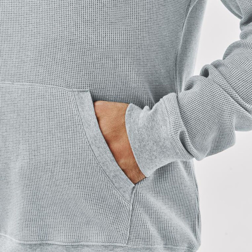 Close-up of light grey waffle-knit hoodie showing kangaroo pocket detail and ribbed cuff, hand tucked in pocket
