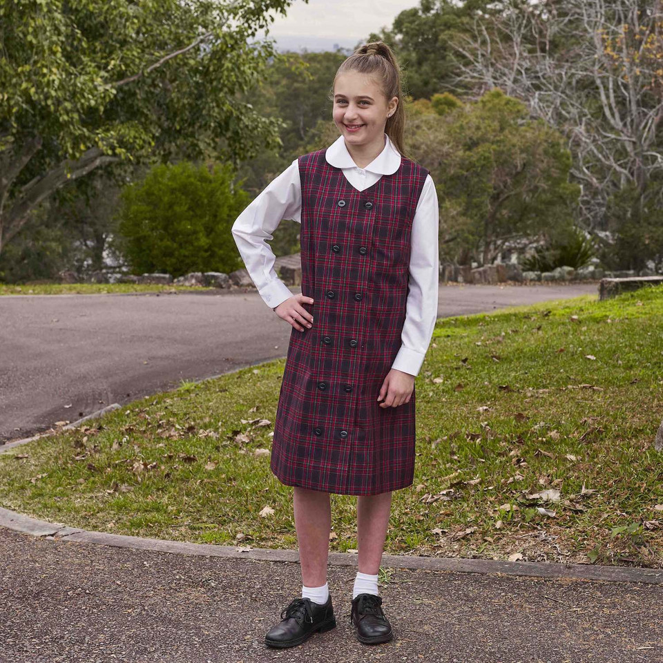 Girl wearing white long sleeve blouse with Peter Pan collar, styled under a red tartan pinafore, outdoor school setting