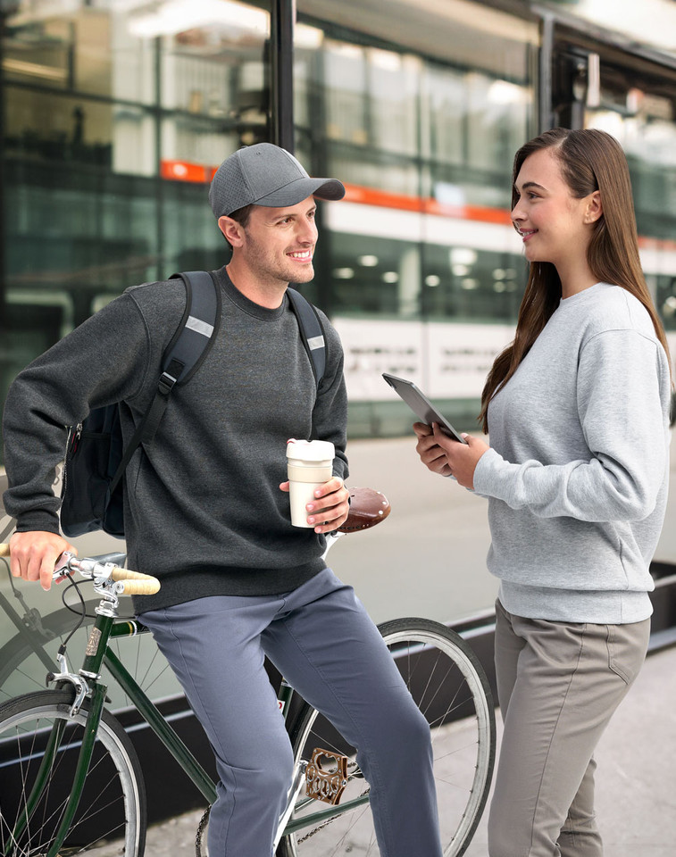 Man and woman lifestyle shot wearing EAGLE cotton-rich sloppy joe sweaters in marl charcoal and grey, urban commuter setting with bicycle and coffee