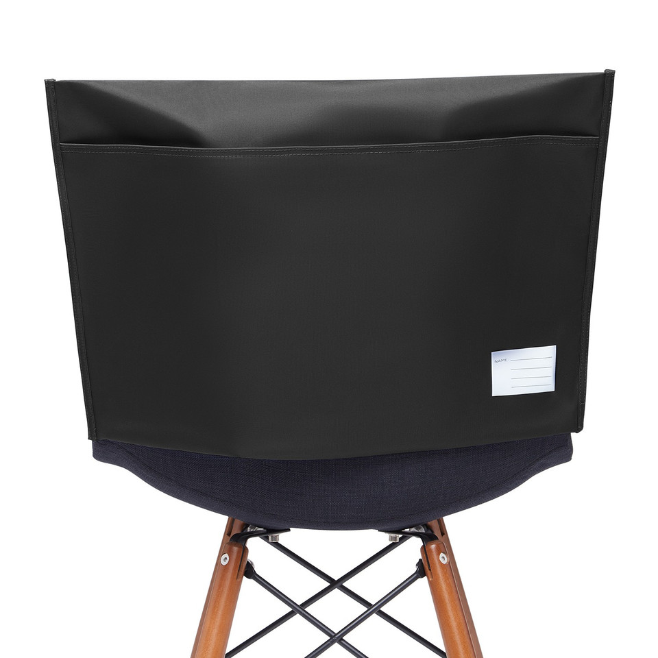 Black classroom chair bag with front pocket and name label card, draped over a wooden chair back