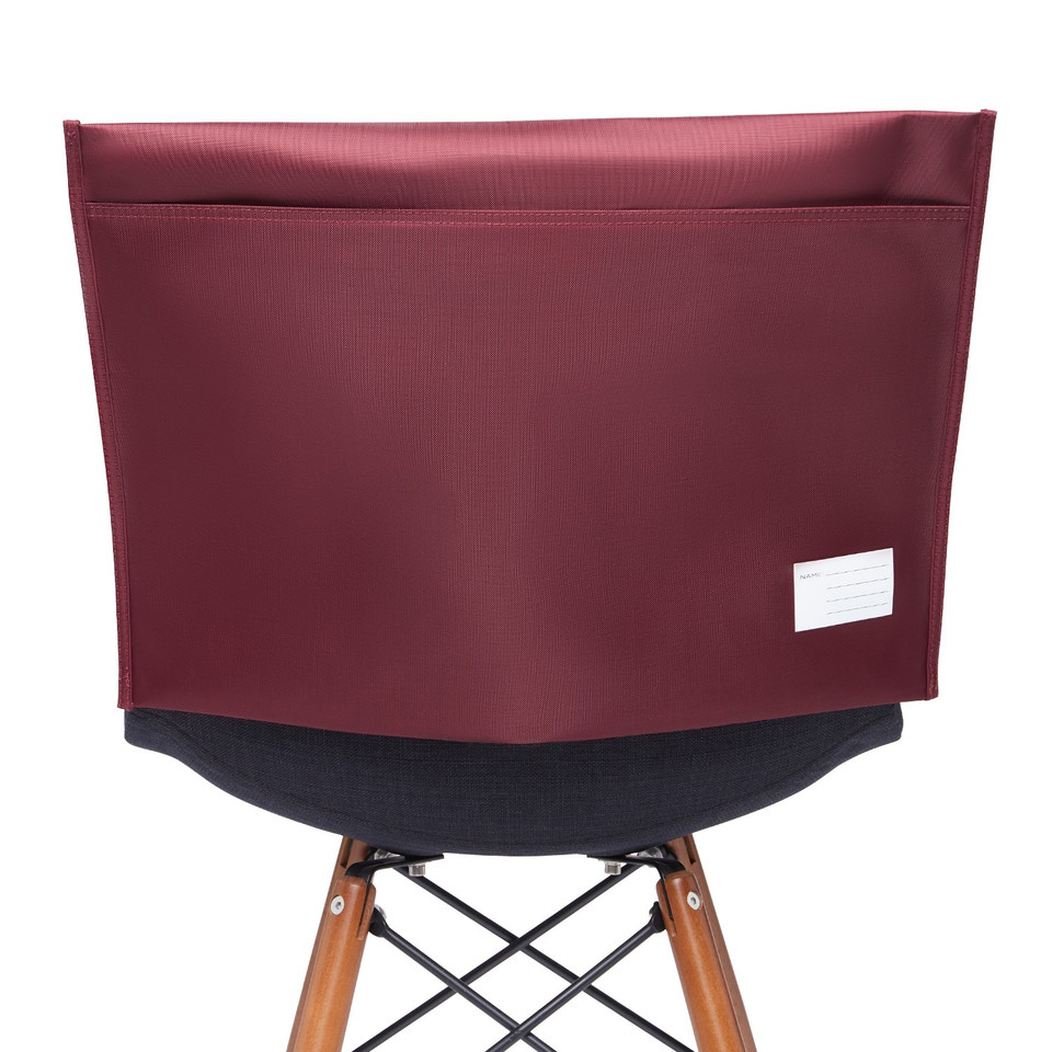 Burgundy structured classroom chair bag with ripstop texture and label, draped over black chair with timber legs