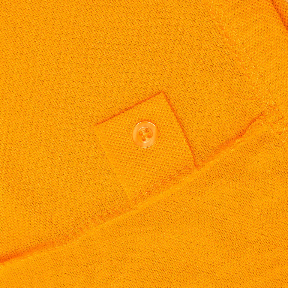 Close-up of amber gold pique polo fabric with tone-on-tone spare button patch detail