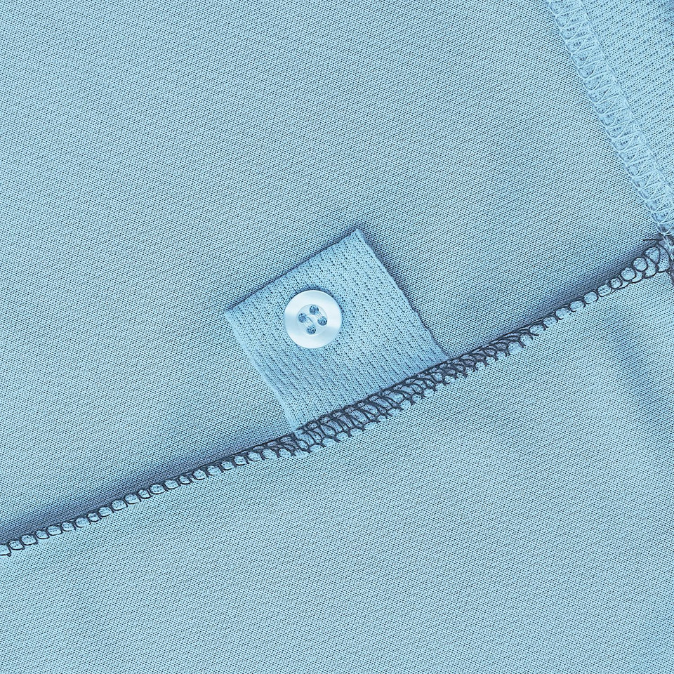 Close-up of powder blue polo placket with four-hole button on woven reinforcement patch and overlock seam detail