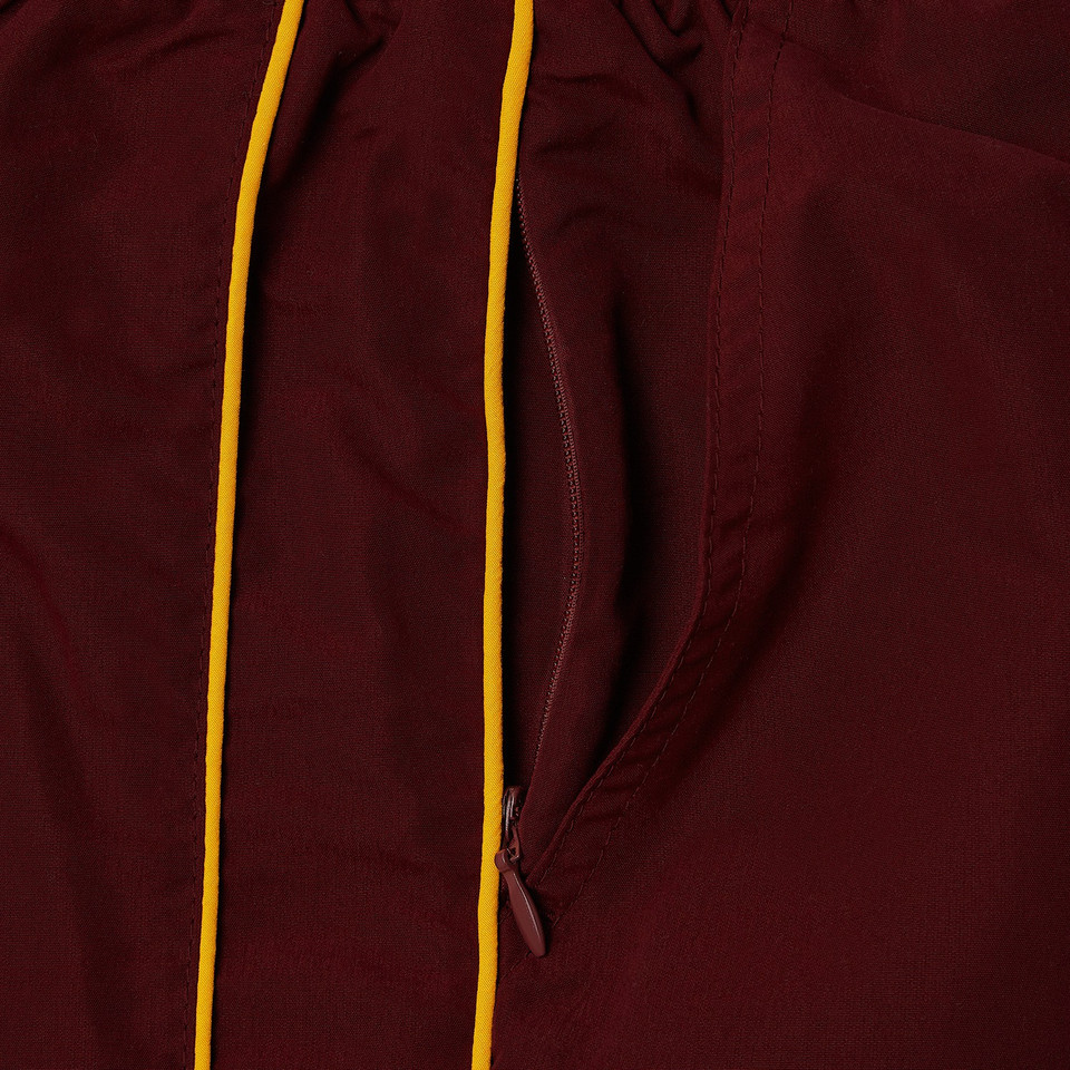 Close-up of maroon microfibre track pants with gold contrast piping and side zip pocket detail