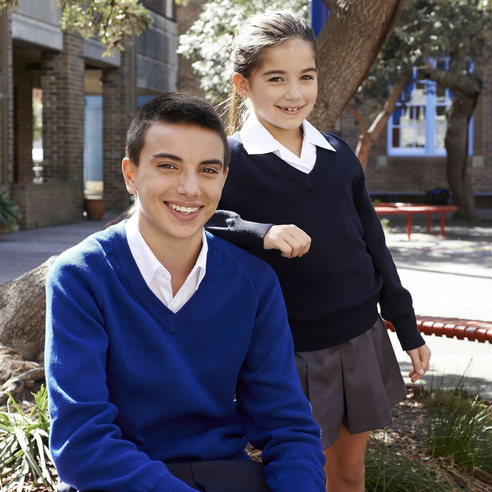 Two students in school setting wearing navy and royal blue V-neck knit jumpers over white collared shirts