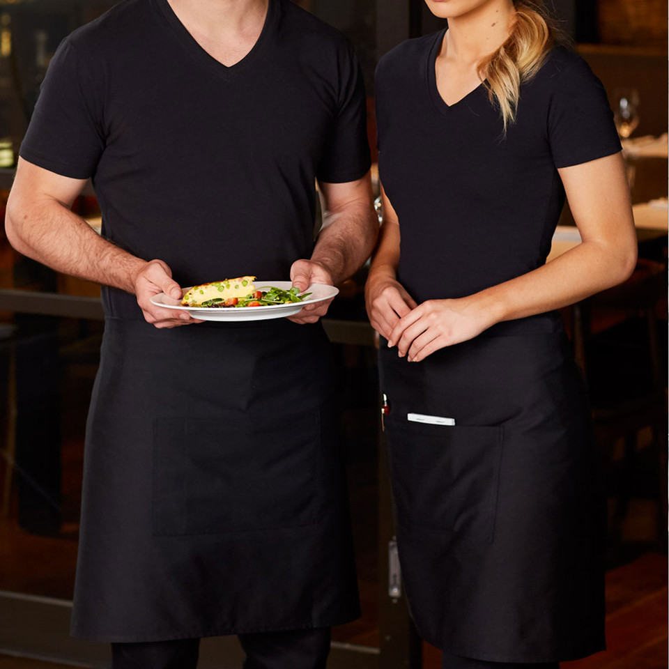 Male and female hospitality staff in black short waist aprons with white pen detail, worn over black v-neck tees in restaurant setting