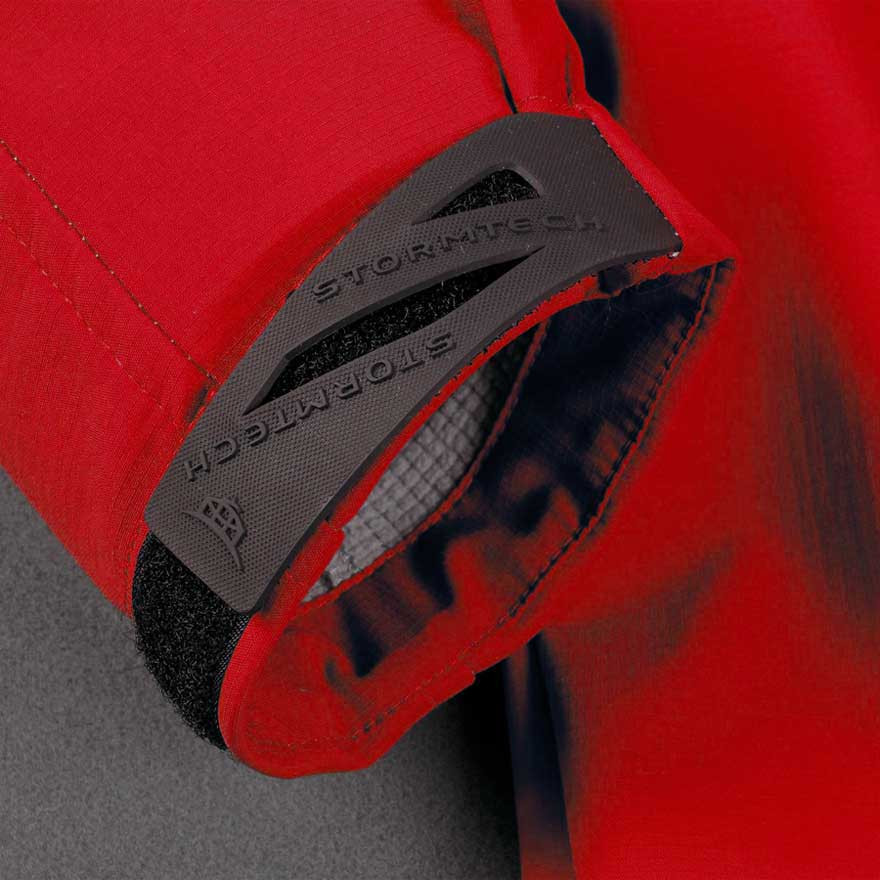 Red softshell jacket with charcoal grey storm flap detail and Velcro adjustable cuff tab