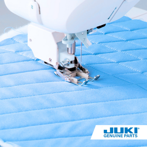 Juki walking foot in action on a computerized sewing machine, stitching smoothly through layered fabric with upper feed dogs preventing bunching and uneven feeding.