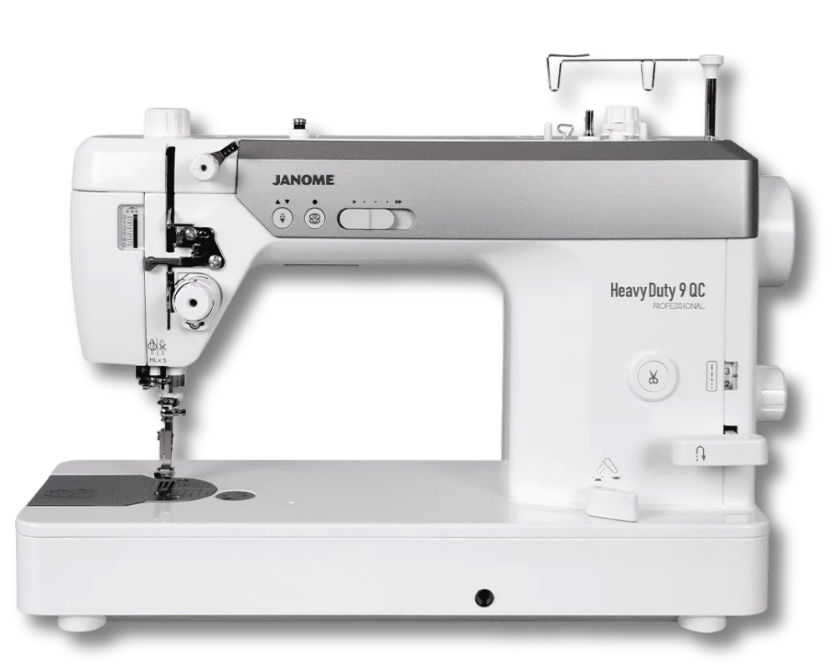 Janome HD9 QCP Heavy Duty 9 QC Professional sewing machine sitting on a wood table beside a red, black, and white patchwork quilt.