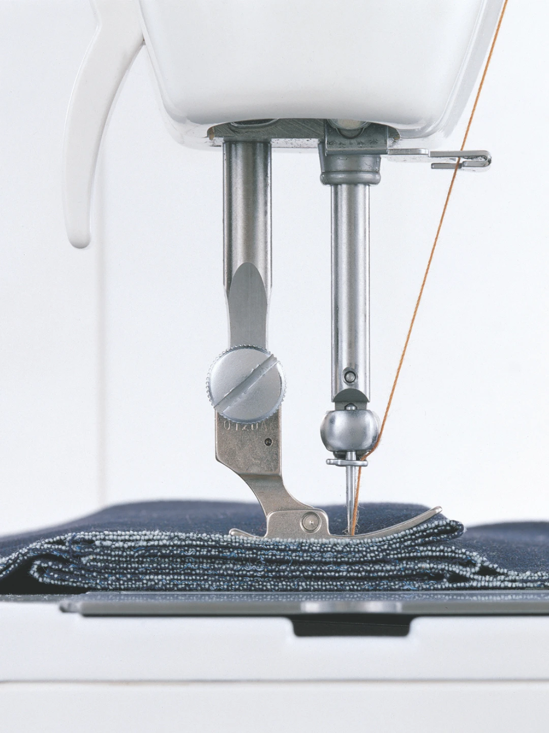 Sewing machine needle stitching through a folded piece of denim fabric.