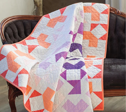 Orange, purple, and white patchwork quilt draped over an antique upholstered chair.