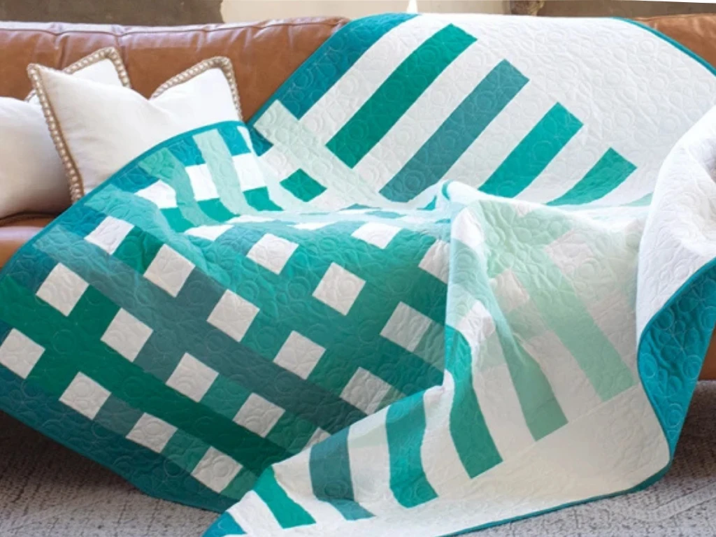 Teal and white striped patchwork quilt folded on a sofa.