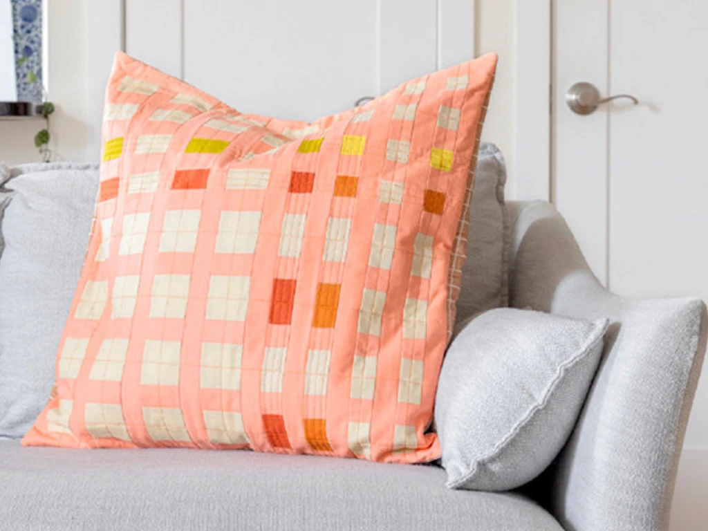 Patchwork throw pillow in orange and cream tones on a gray sofa.