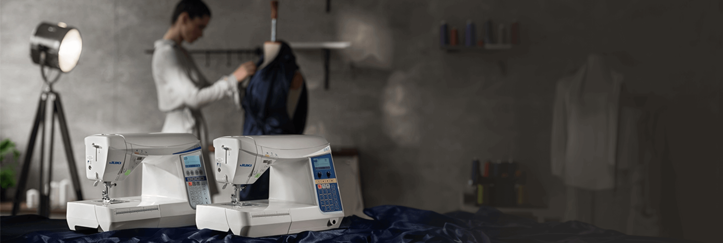 Image of two Juki computerized sewing machines in a workplace. A female tailor or seamstress is in the background.