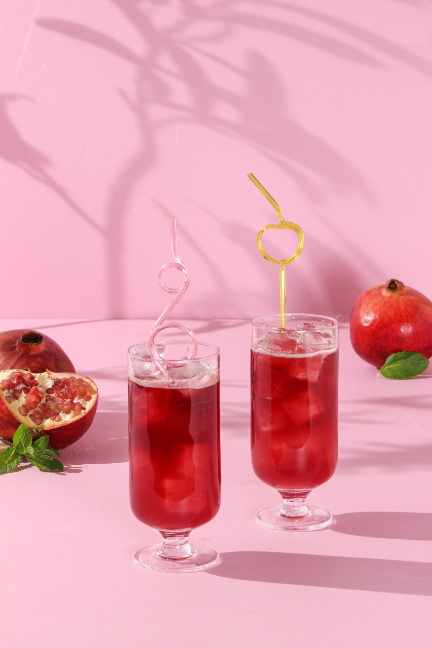 bright red cocktail on a pink background, with a pastel straw and pomegranate