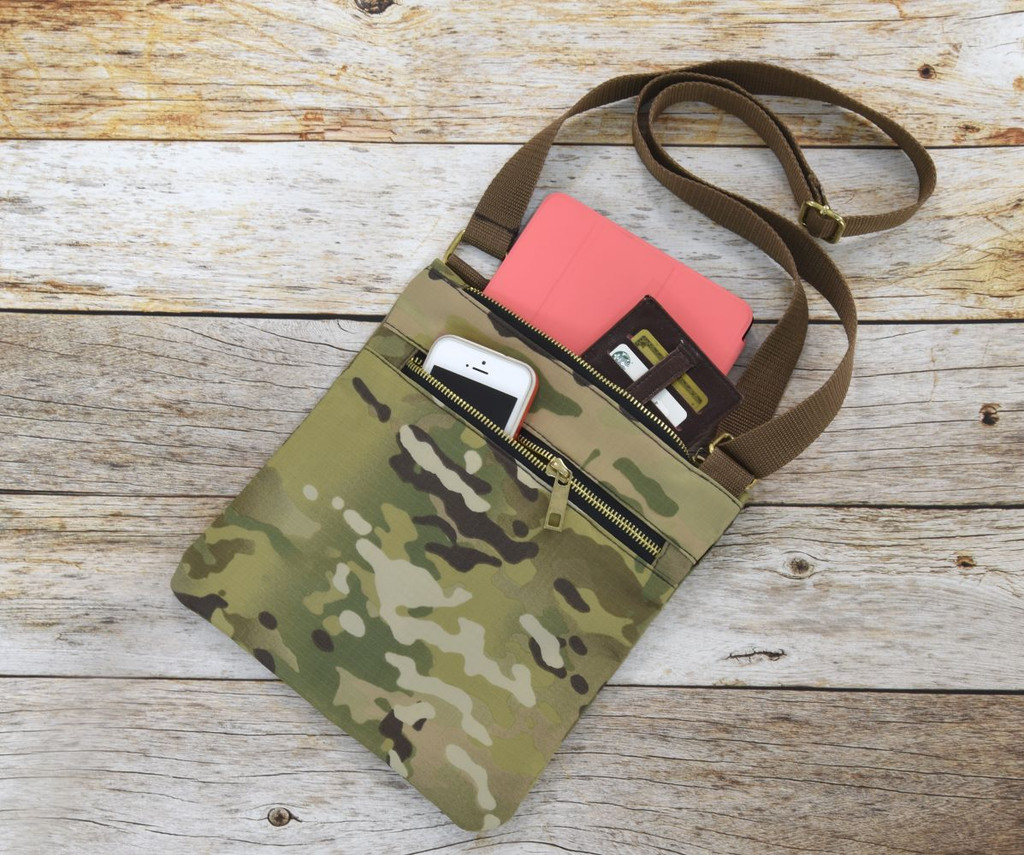 MultiCam® Crossbody Bag shown against wood background with tablet and wallet inside main compartment and phone in front pocket.