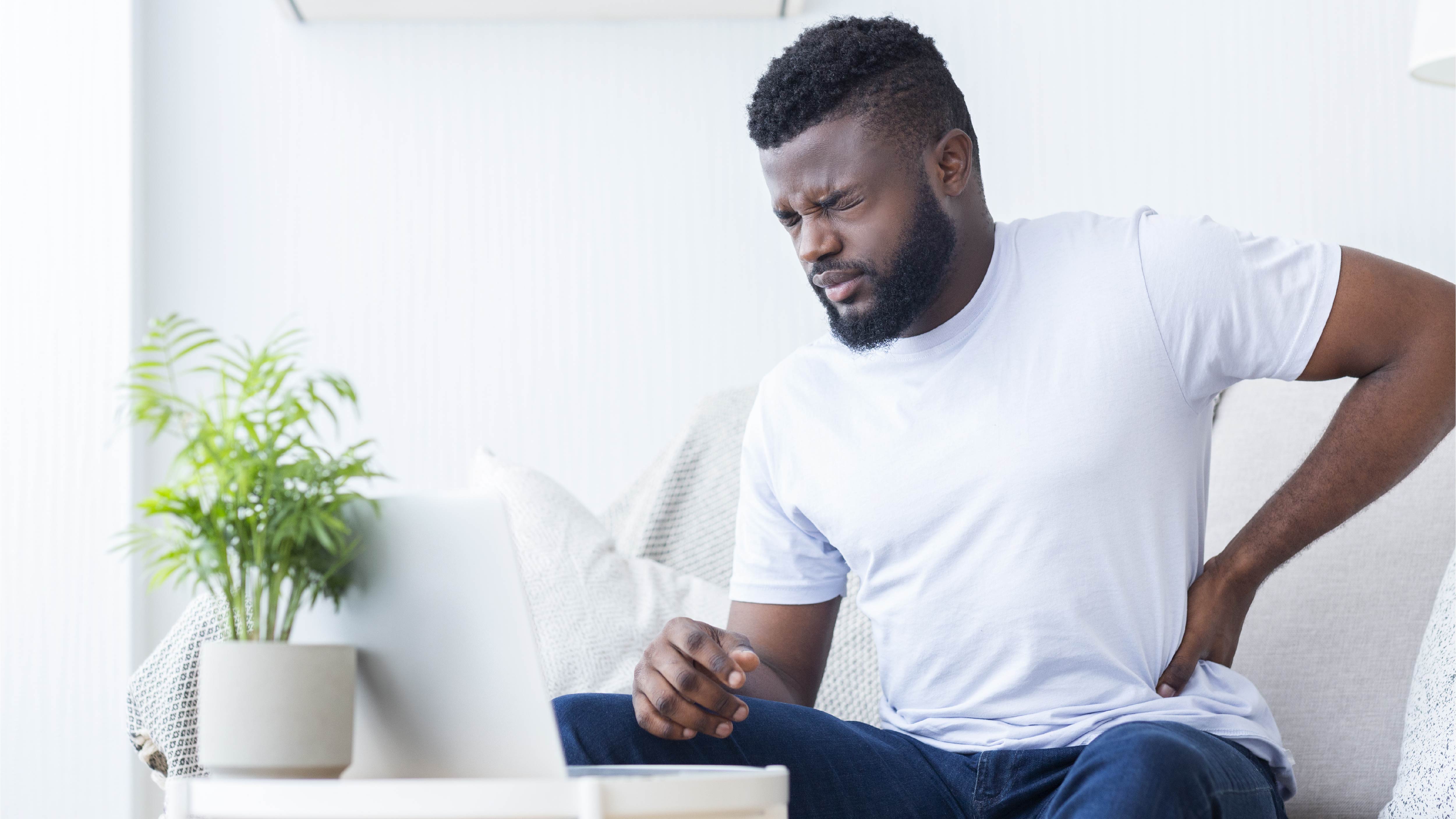 Person clutching side of waist indicating back pain while seated on a sofa