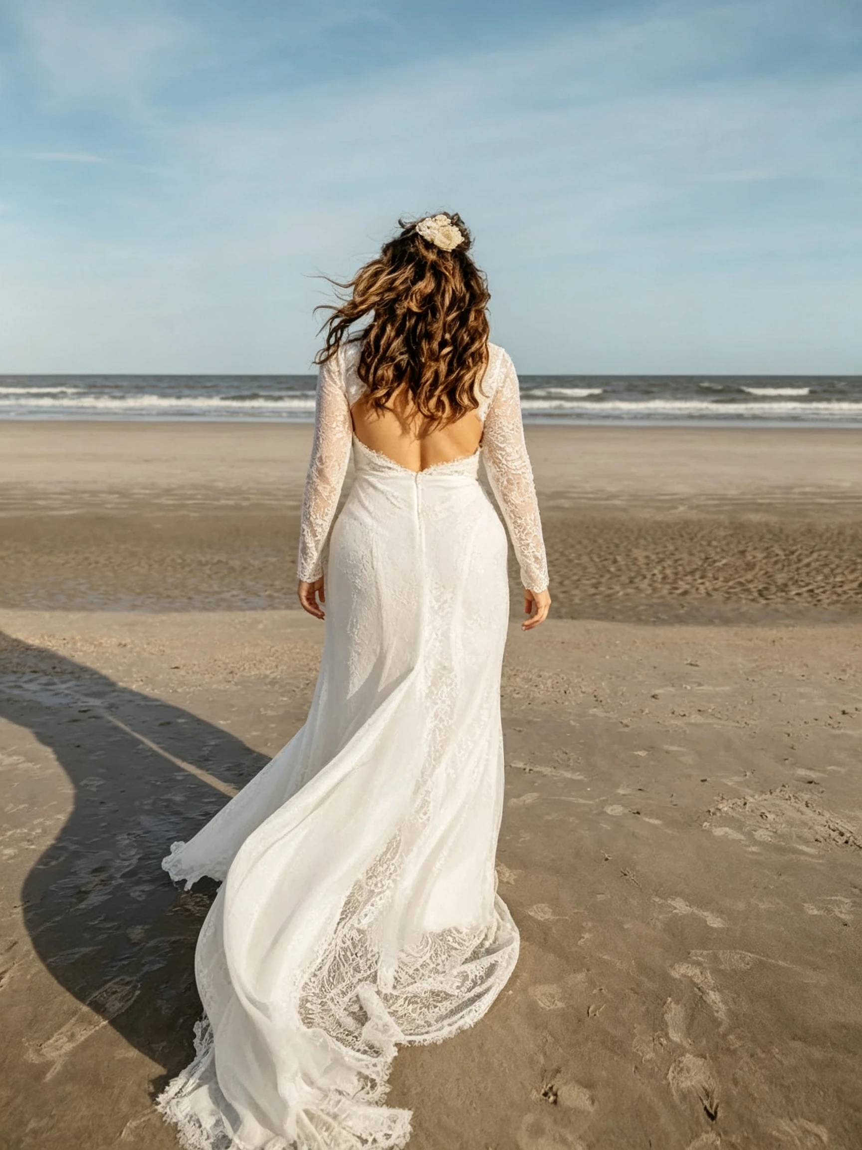 Bride walking away showing long train of lace wedding dress on beach