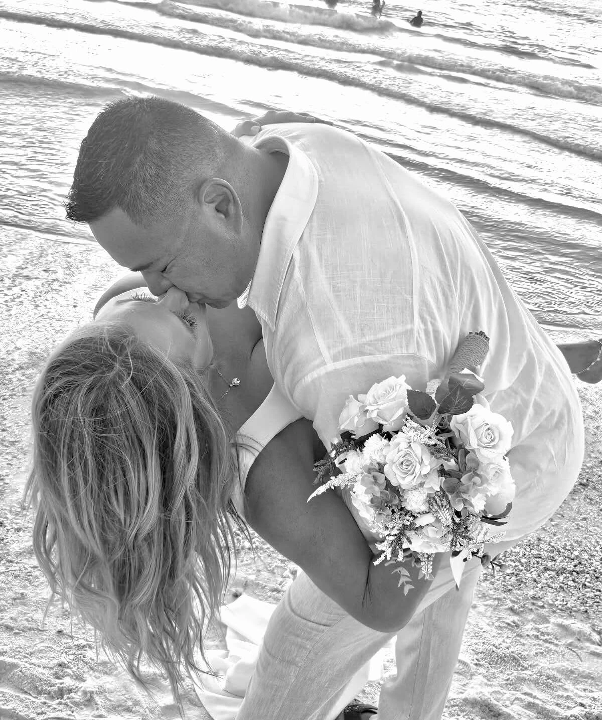Black and white wedding photograph of bride and groom at the surf in a white mermaid dress