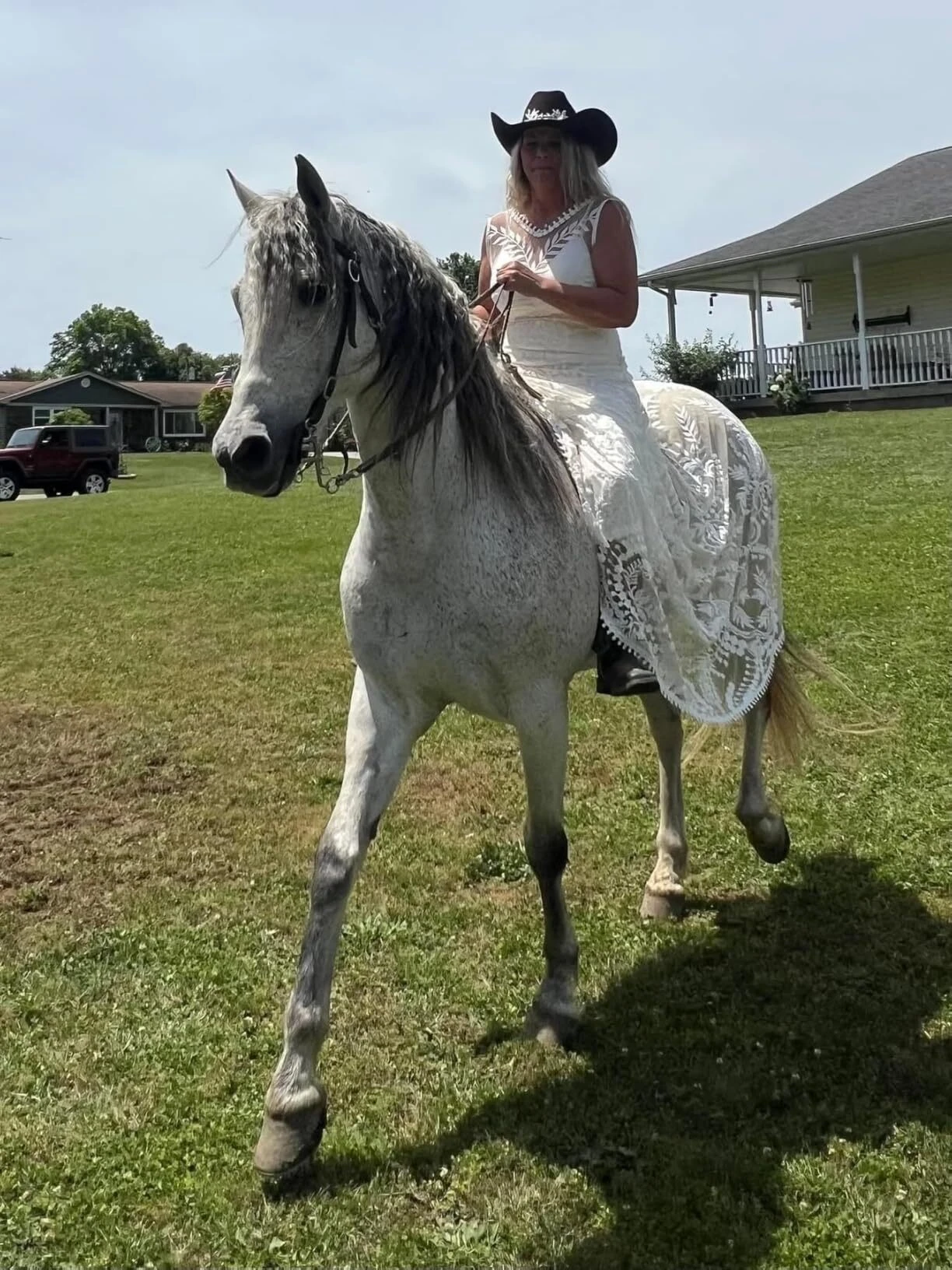 Bride wearing a boho lace wedding dress while riding a white horse across a grass field
