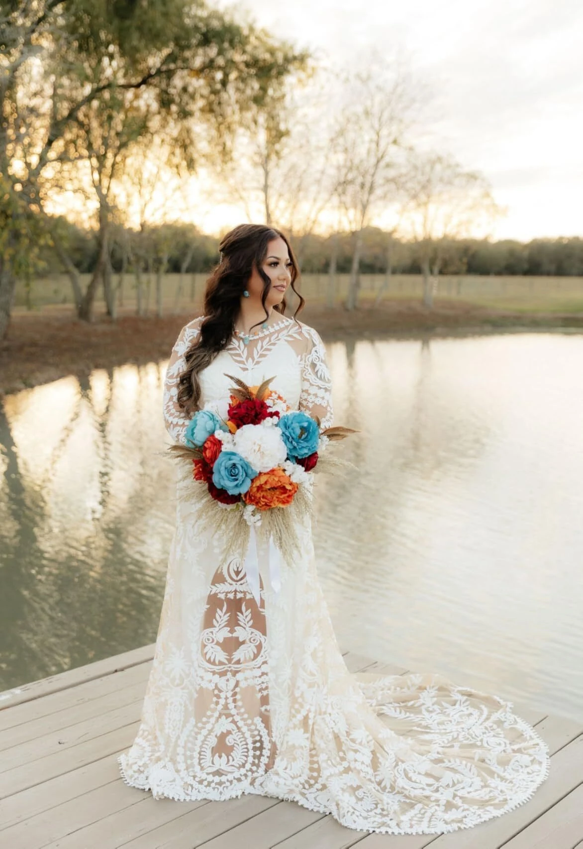 Bride wearing lace wedding dress standing on lake dock
